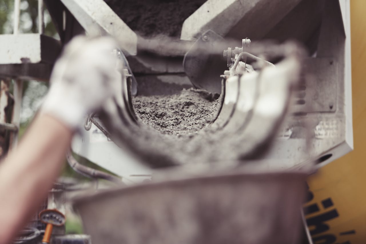 Close-up of concrete being poured from a mixer truck at a construction site with a workers hand visible.